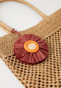 Gewebe-Stroh-Handtasche mit zwei strukturierten Griffen. Auf der Vorderseite befindet sich eine florale Verzierung in Rot und Orange. Offenes Webdesign.