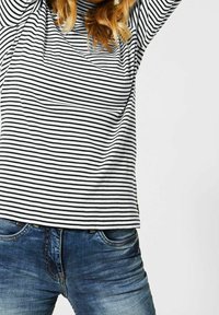 Černobílý pruhovaný top s dlouhým rukávem a volným střihem, kombinovaný s modrými riflovými džínami s klasickým pětikapsovým designem.