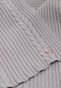 Pull en maille gris clair avec texture côtelée et détails en câble. Il présente un petit accent de logo doré sur le côté.