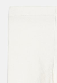 Leggings blancs côtelés avec une texture lisse et une taille élastique, présentant une coupe slim et sans motifs ni accents visibles.