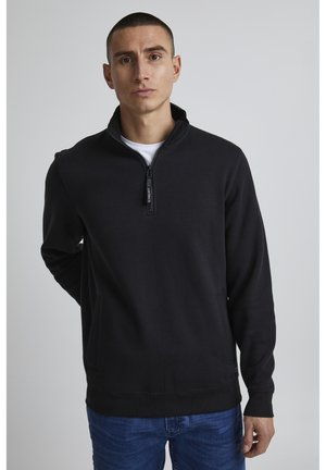 Sweat-shirt noir à col zippé avec une texture douce, des manches longues et des poches latérales. Présente un détail de zip de marque subtile sur le col.
