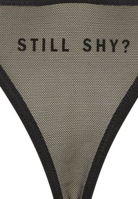 String en mesh noir avec intérieur beige clair et texte « STILL SHY ? » imprimé en noir gras. Taille fine et bords sans coutures.