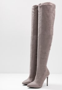 Botas grises por encima de la rodilla en suave ante con punta afilada y tacón de aguja, que presentan una textura suave y detalles de diseño mínimos.