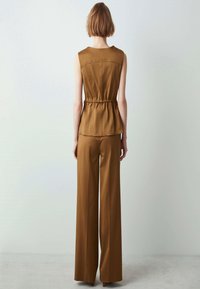 Top marrone senza maniche con vita stretta e texture liscia, abbinato a pantaloni larghi a vita alta nello stesso materiale e colore.