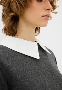 Grauer Pullover mit einem breiten weißen Kragen. Hat eine weiche Textur, eine enganliegende Passform und sichtbare Nähte am Kragen. Keine weiteren Details.