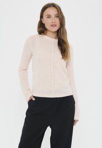 Light pink sweater in a soft material, featuring long sleeves, a round neckline, and a central cable-knit pattern. Paired with black trousers.