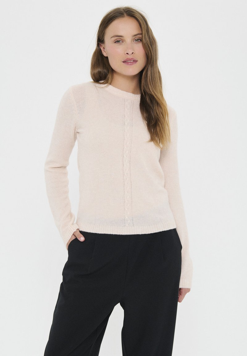 Light pink sweater in a soft material, featuring long sleeves, a round neckline, and a central cable-knit pattern. Paired with black trousers.