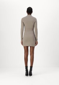 Jasnobrązowa, długa sukienka bodycon z wysoką szyją, gładką fakturą, dopasowanym fasonem i mini długością. Połączona z czarnymi botkami za kostkę.