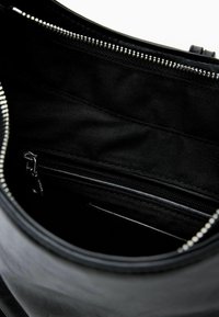 Vnútro čiernej koženej kabelky so zipsovou vnútornou kapsou a hladkou, netextúrovanou látkovou podšívkou. Pozdĺž horného okraja viditeľný kovový zips.