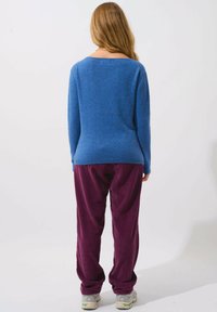 Blauer gestrickter Pullover mit lockerer Passform und weitem Ausschnitt, kombiniert mit bordeauxroten Cordhosen. Der Stoff ist weich; die Hosen haben eine vertikale Rippung.