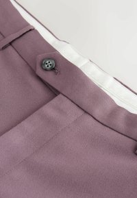 Zbliżenie na pas spodni z fioletowawobrązowego materiału z czarnym guzikiem i białą podszewką od wewnątrz.