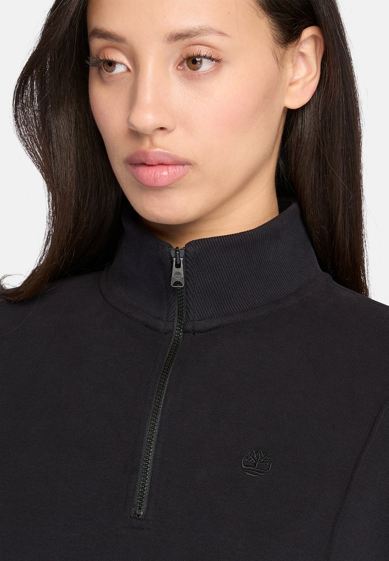 Felpa nera con zip caratterizzata da un collo alto, un colletto a coste, un tessuto morbido e un piccolo logo discreto sul petto.