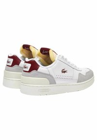 Sneaker bianche con tomaia in pelle liscia, accentuazioni in suede grigio, tacco rosso, dettagli forati e suola spessa bianca. Presente il marchio Lacoste.