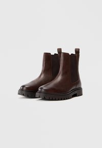 Bottines Chelsea en cuir marron avec panneaux élastiques sur les côtés, bout rond et semelle en caoutchouc noir épaisse dotée d'un motif de traction pour l'adhérence.