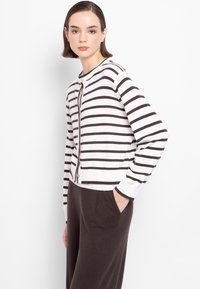 Cardigan lavorato a maglia con righe orizzontali marroni e bianche, colletto rotondo, chiusura a bottoni e polsini a costine, abbinato a pantaloni scuri.