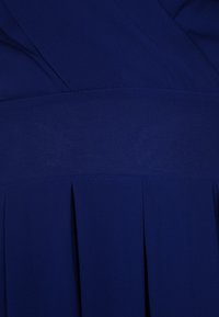 Gros plan d’un tissu bleu foncé avec des plis cousus et des détails pliés, probablement une partie d’un vêtement.