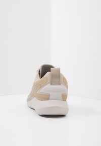 Beige och ljusgrå sneakers med rundad form, slät läderöverdel, texturerade detaljer och en dragflik vid hälen.