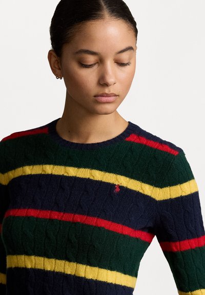 Pull en tricot avec des rayures horizontales vertes, marines, rouges et jaunes. Texture en torsades avec un petit logo sur la poitrine.
