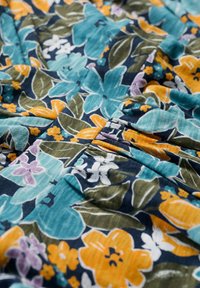 Blumiger Stoff mit großen blauen, orangefarbenen, lila und weißen Blumen auf einem dunkelgrünen und marineblauen Hintergrund mit strukturiertem Finish.