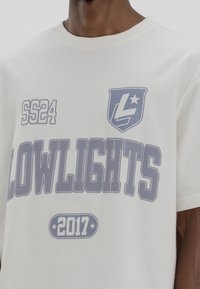 Bílý bavlněný tričko s potiskem "SS24" a "LOWLIGHTS 2017" v světle šedé typografii, doplněné logem ve tvaru štítu. Krátké rukávy, kulatý výstřih.