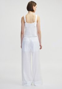 Weißes, kurzes Tanktop mit breiten Trägern und Knopfakzenten, kombiniert mit locker sitzenden, durchsichtigen weißen Hosen mit elastischem Bund.
