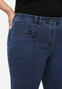 Jeans de mezclilla azul oscuro con un bolsillo con cremallera en la parte frontal, costuras reforzadas y un diseño tradicional de cinco bolsillos.