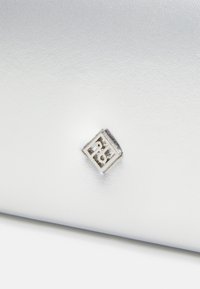 Srebrna metaliczna kopertówka o gładkiej fakturze z kwadratowym logo wygrawerowanym z napisem "TB". Projekt jest elegancki i minimalistyczny.