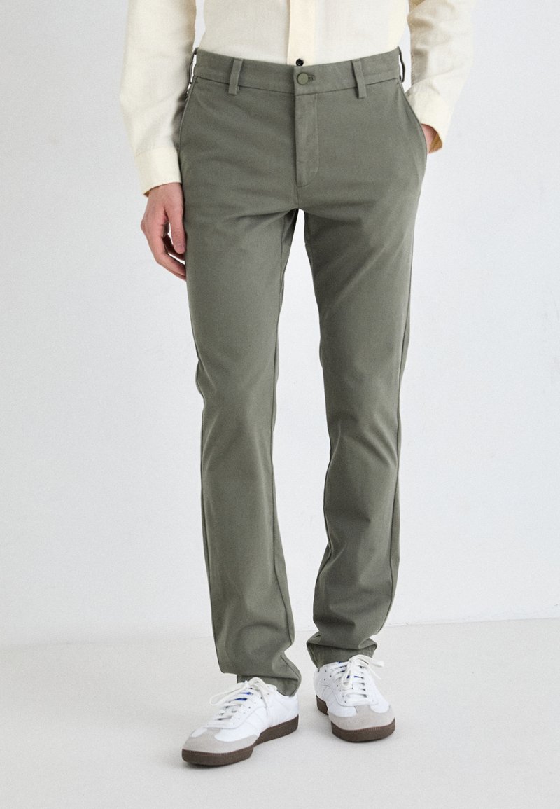 Green cotton trousers with a straight-leg design, featuring a front button closure and side pockets, paired with white sneakers.
