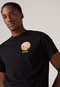 Tricou din bumbac negru, cu un logo grafic rotund ce prezintă un peisaj pastelat și textul "Levis". Mâneci scurte și decolteu tip crew.