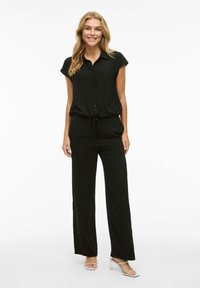 Fekete overáll rövid ujjakkal, gombos záródással, rugalmas derékkal és széles lábakkal. Könnyű, sima tapintású anyag.