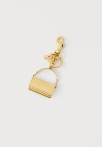Χρυσό μπρελόκ σε σχήμα μικρής τσάντας με κυρτή λαβή, κούμπωμα με καβούρι και δύο συνδεδεμένα δαχτυλίδια σε λευκό φόντο.