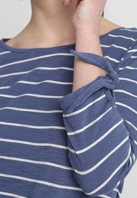 Marinblårandig topp med vita horisontella linjer, med en lös passform och knytdetaljer vid ärmarna, tillverkad av ett mjukt tyg.