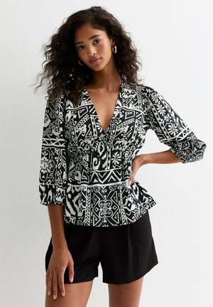Blusa a righe bianco e nero con scollatura a V profonda, maniche ¾ e dettaglio in vita elastico, abbinata a pantaloni corti neri.