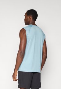 Ανοιχτό μπλε αθλητικό τοπ με στρογγυλή λαιμόκοψη και λείο ύφασμα που απομακρύνει την υγρασία. Συνοδεύεται από μαύρο σορτς με ελάχιστη λογότυπο λεπτομέρεια.