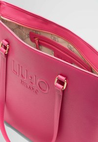 Borsa a spalla sintetica rosa con superficie testurizzata, logo in rilievo, due manici e un vano con cerniera foderato in tessuto pattern.