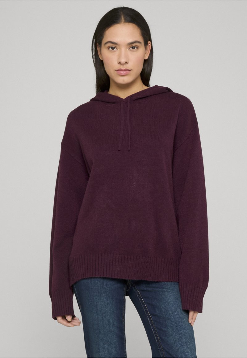 Sweat à capuche couleur prune avec une coupe décontractée, poignets et ourlet côtelés. Tissu texturé à finition douce, associé à un jean bleu.