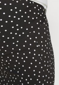 Leggings pretas com bolinhas brancas, feitas de tecido elástico, apresentando um design ajustado com uma textura suave e detalhes de costura.