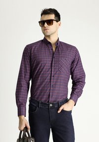 Camicia a maniche lunghe a quadri in navy e bordeaux, con colletto button-down e taschino sul petto, abbinata a jeans scuri e occhiali da sole.
