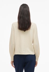 Beežikas pikkade varrukatega top lõdva lõikega, ümarate servadega ja detailsete puffvarrukatega; sile tekstuur, soonikkoes mansetid ja seljatikk.