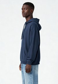 Námornícky modrá mikina z mäkkého materiálu s klokaním vreckom, kapucňou na sťahovanie a rebrovanými manžetami. Nosí sa s svetlomodrými džínami.