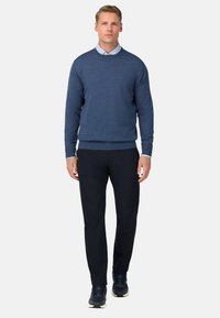 Sinine ümmarguse kaelusega sviiter, mis on valmistatud kudumiskangast, koos tumedate pükste ja spordijalatsitega. Sile tekstuur, mugav lõige ja soonikkoes varrukate otsad.