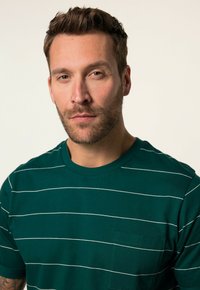 Camiseta verde a rayas con rayas blancas horizontales, cuello redondo, mangas cortas y un bolsillo en el pecho izquierdo. Material de algodón suave.
