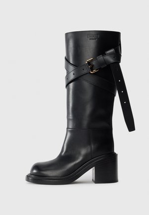 Black leather knee-high boot with block heel, decorative strap with gold buckle, and embossed Moschino Milano logo on shaft.