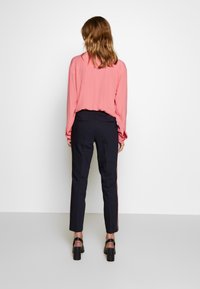 Dlouhý rukáv, světle růžová blůza v kombinaci s upnutými navy kalhotami s červenými pruhy po stranách; boty jsou černé sandály na blokovém podpatku.