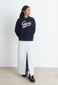 Navy hooded sweatshirt with white 'Gant' logo, paired with a light blue maxi skirt featuring a front slit, and black athletic shoes.