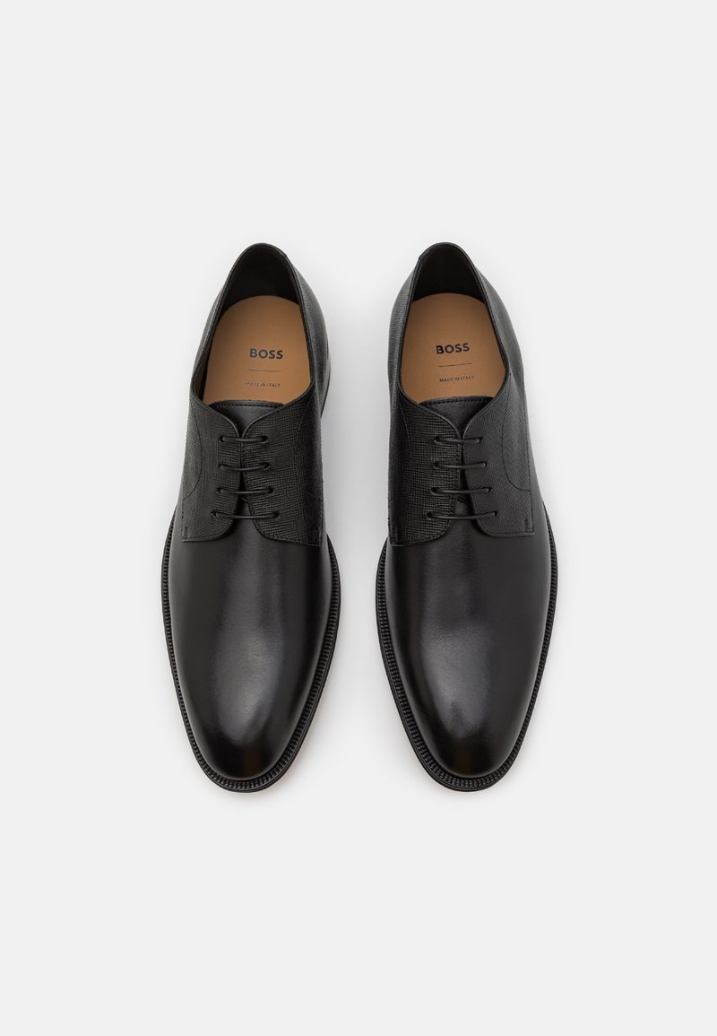 Chaussures en cuir noir à lacets avec une finition lisse et des panneaux texturés. Forme de bout arrondi et semelle noire contrastante. L'intérieur présente le logo de la marque.
