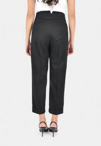 Pantaloni neri su misura con vita alta, caratterizzati da una texture liscia, gambe dritte e orli risvoltati, abbinati a tacchi a stiletto neri con cinturini.