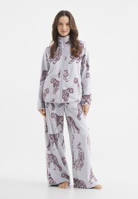 Zestaw dresowy z polaru zawierający kurtkę na zamek i spodnie o szerokiej nogawce. Jasnoszary z powtarzającym się burgundowym wzorem w tygrysa. Miękka tekstura.