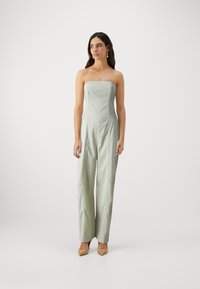 Combinaison sans manches, verte claire avec un corsage ajusté, des jambes larges et des détails de couture subtils. Portée avec des talons aiguilles beiges.