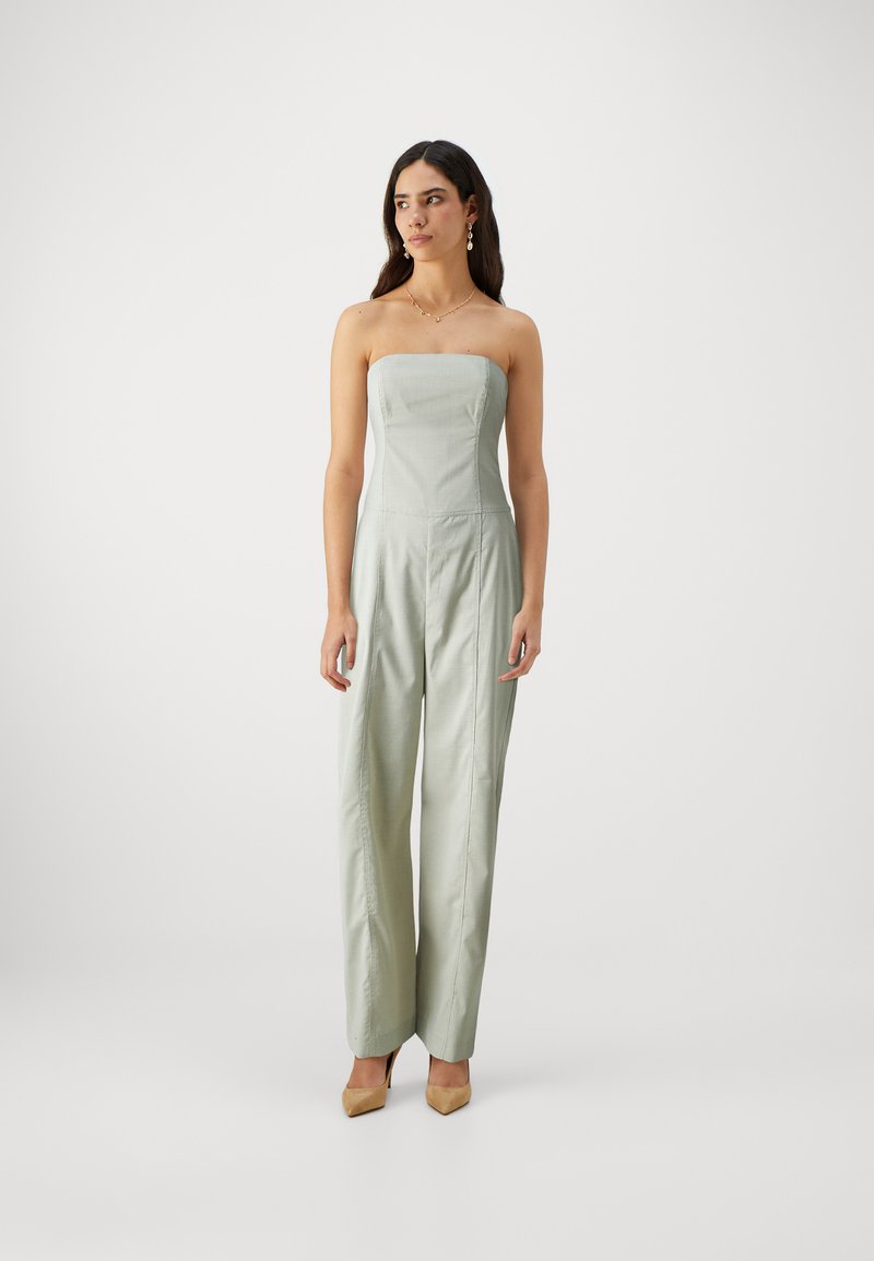 Combinaison sans manches, verte claire avec un corsage ajusté, des jambes larges et des détails de couture subtils. Portée avec des talons aiguilles beiges.